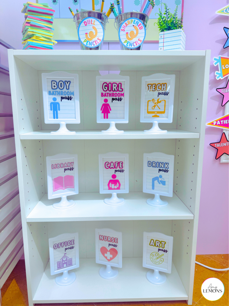 Nine classroom hallway passes in white picture frames displayed on a bookshelf, including bathroom, nurse, library, and art passes for a simple classroom  organization idea.